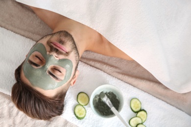 Young man with clay mask on his face in spa salon, above view