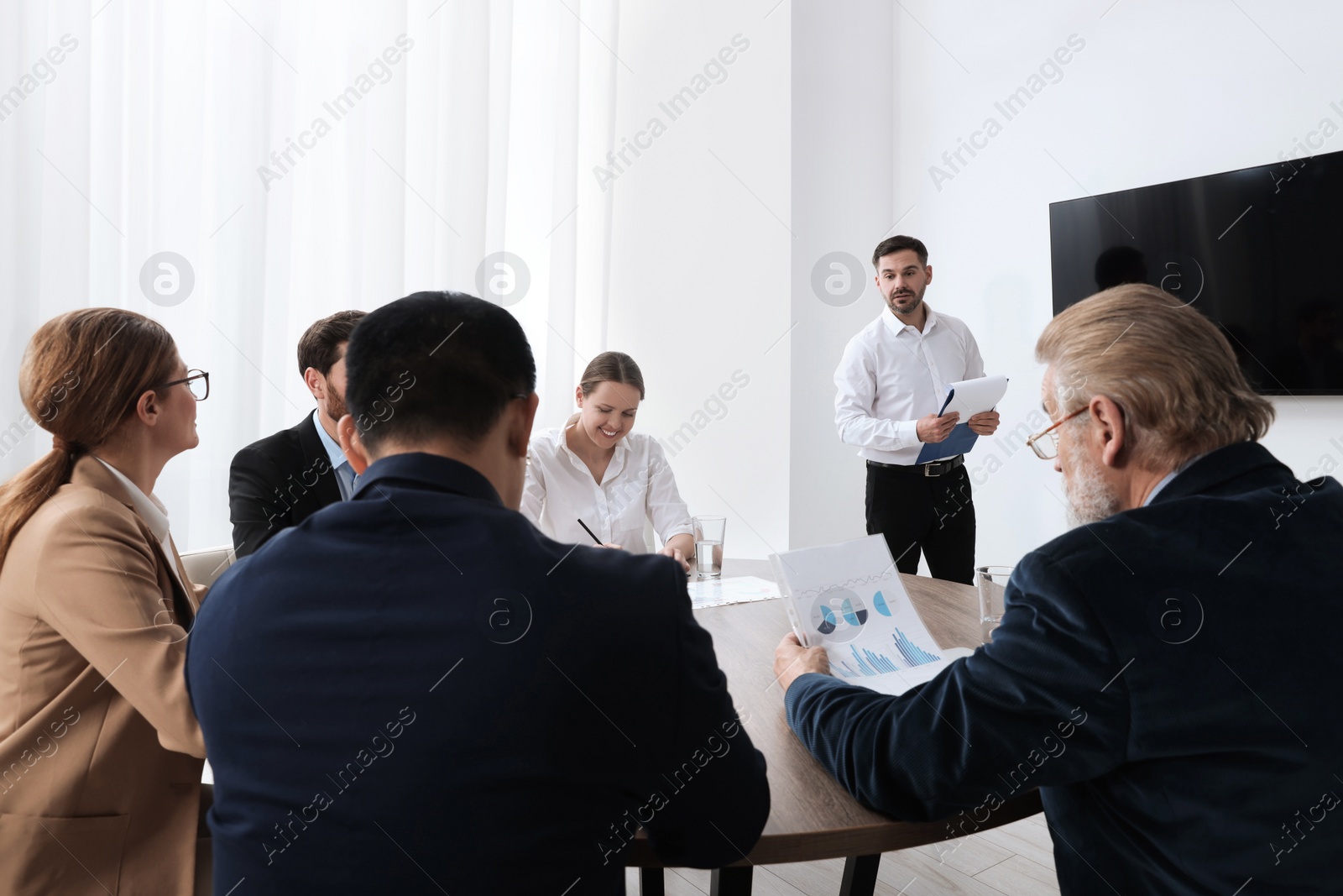 Photo of Business conference. Group of people listening to speaker report near tv screen in meeting room