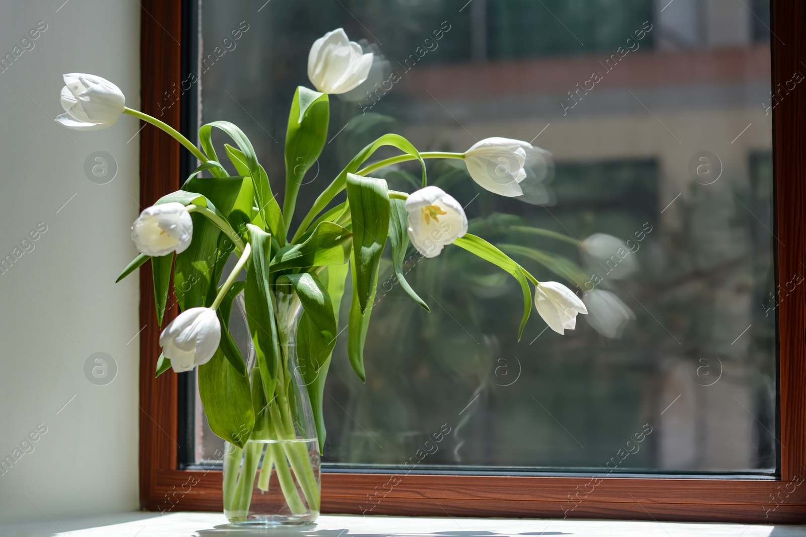 Photo of Bouquet of beautiful white tulip flowers in glass vase on windowsill indoors