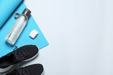 Photo of Exercise mat, bottle of water, wireless earphones and shoes on light grey background, flat lay. Space for text