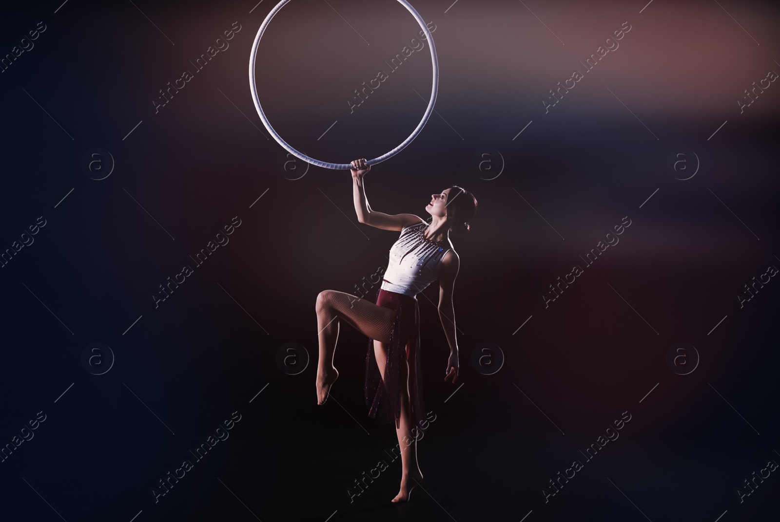 Photo of Young woman performing acrobatic element on aerial ring indoors