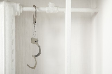 Handcuffs hanging on radiator near white wall indoors