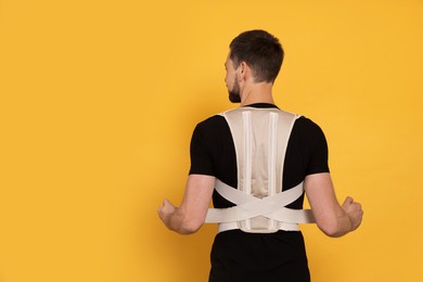 Photo of Man with orthopedic corset on orange background, back view. Space for text