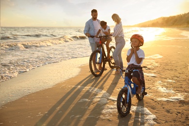 Happy family with bicycles on sandy beach near sea
