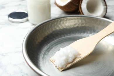 Photo of Frying pan with coconut oil and wooden spatula on white marble table, closeup. Healthy cooking