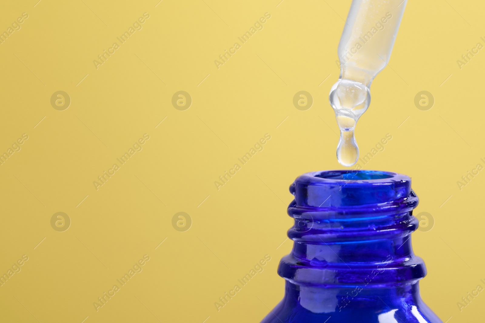 Photo of Dripping serum from pipette into bottle on yellow background, closeup. Space for text