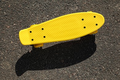 Photo of Modern yellow skateboard on asphalt road outdoors, top view