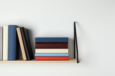 Photo of Wooden shelf with many hardcover books on white wall