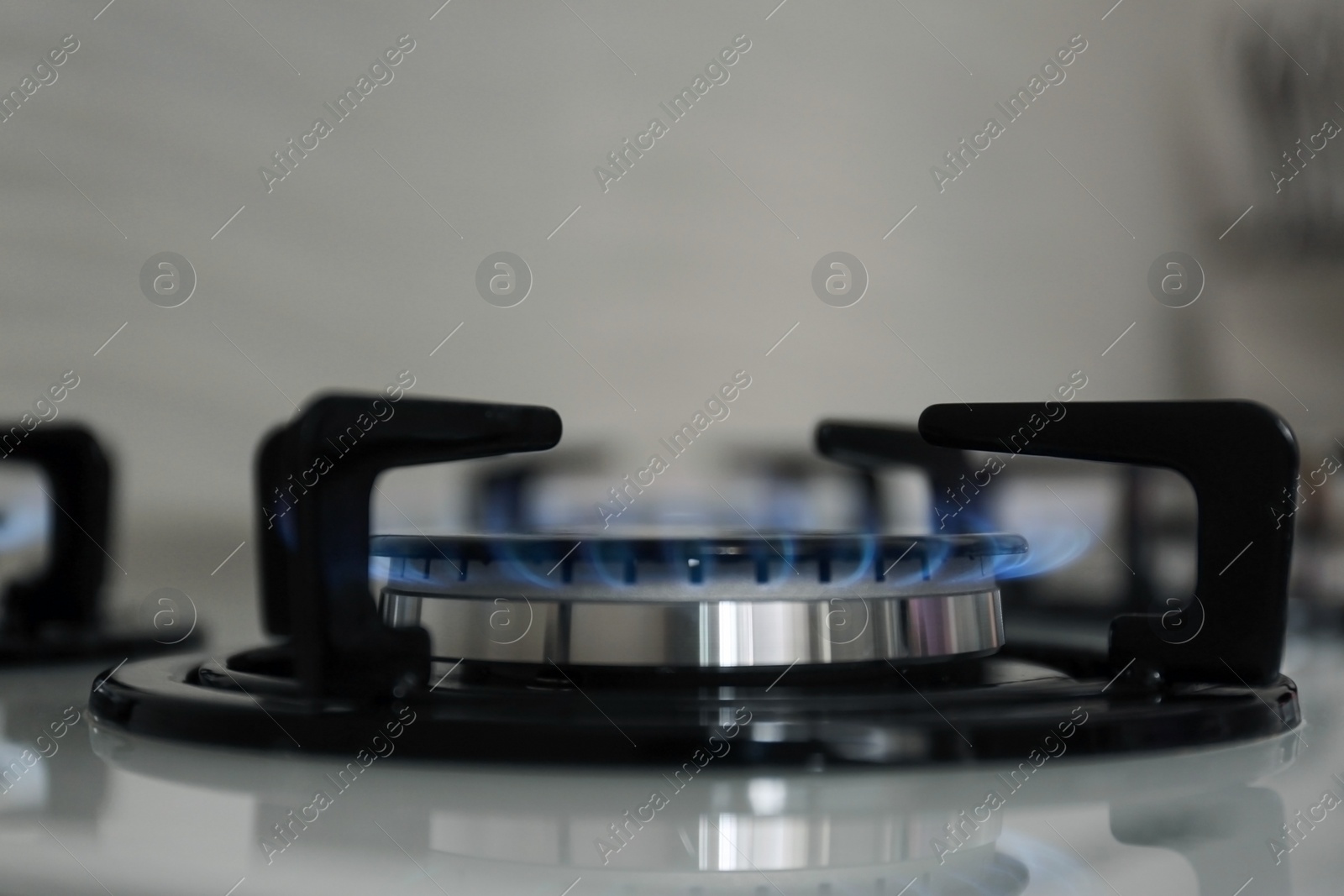 Photo of Gas burner with blue flame on modern stove, closeup. Space for text