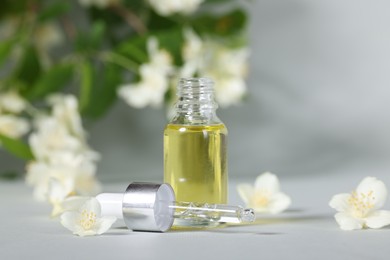 Photo of Essential oil in bottle, beautiful jasmine flowers and pipette on grey background, closeup