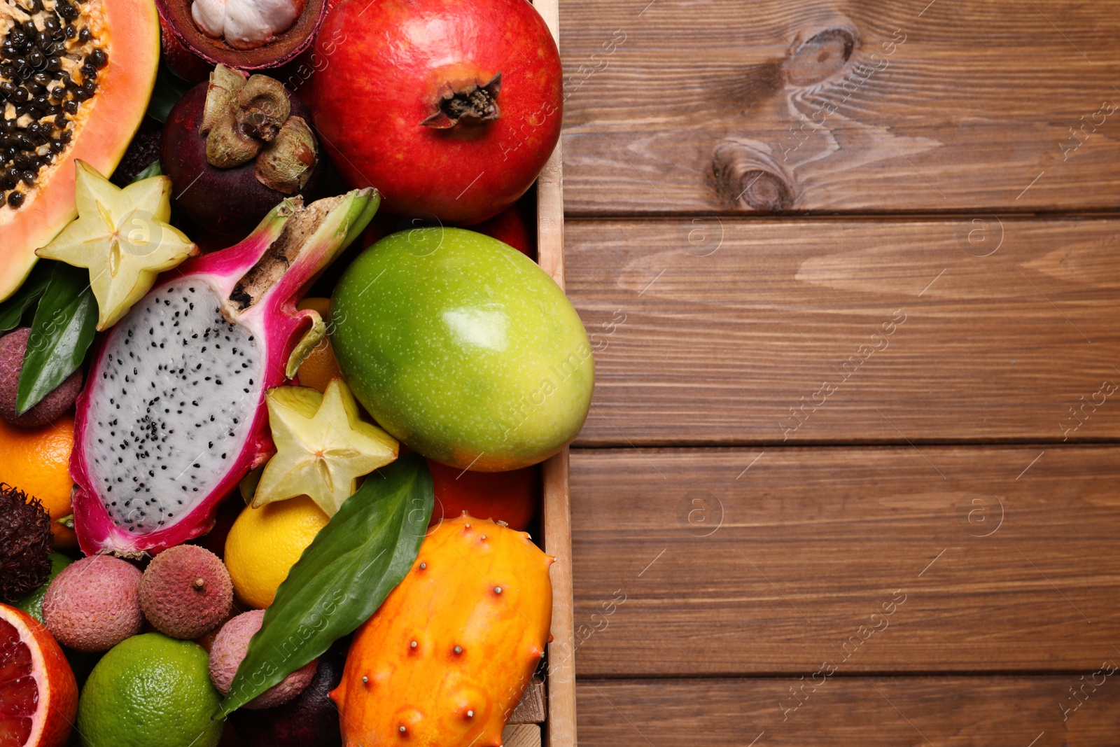 Photo of Crate with different exotic fruits on wooden table, top view. Space for text