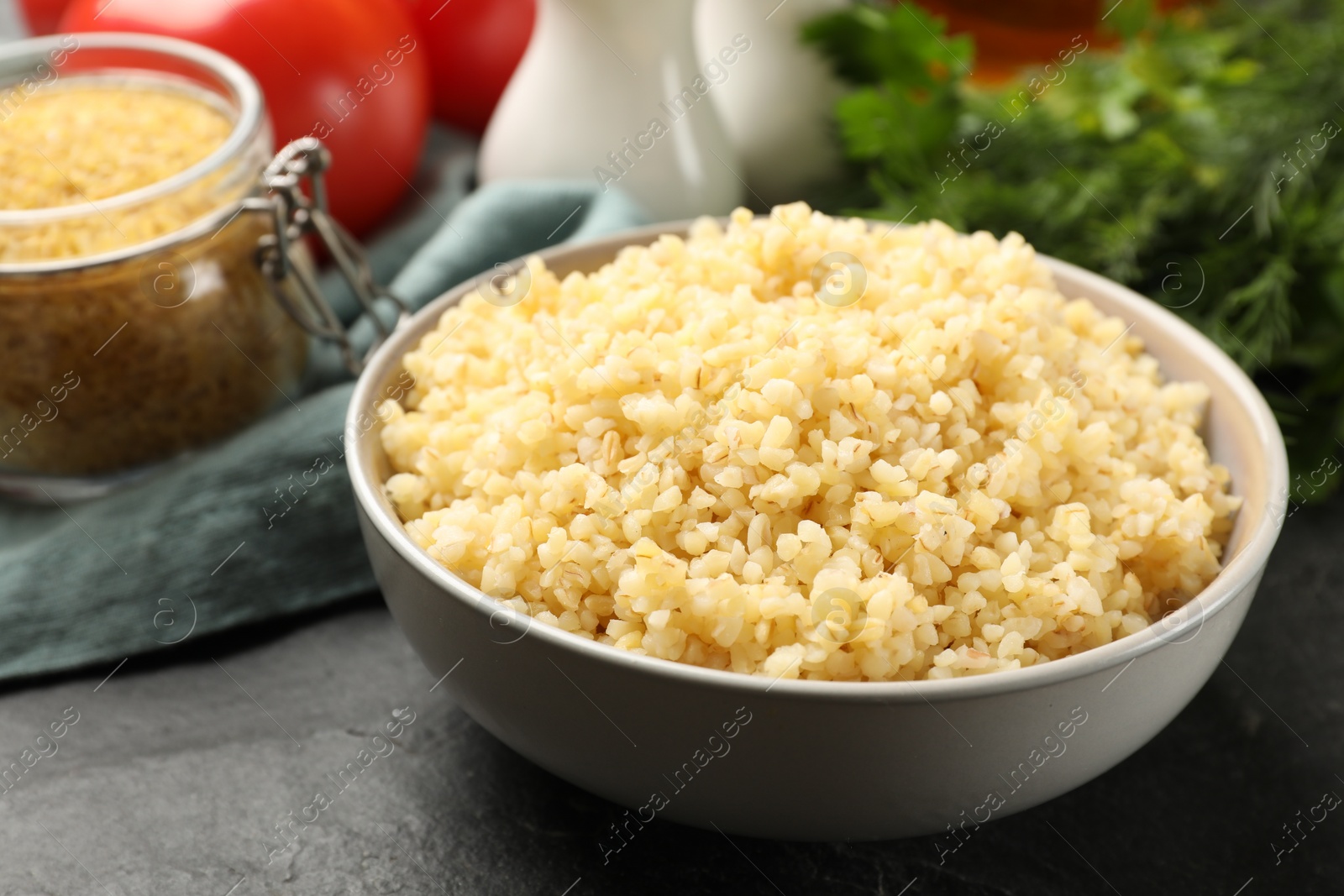 Photo of Delicious bulgur in bowl on black table, closeup