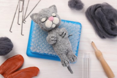 Photo of Felted cat, wool and different tools on light wooden table, flat lay