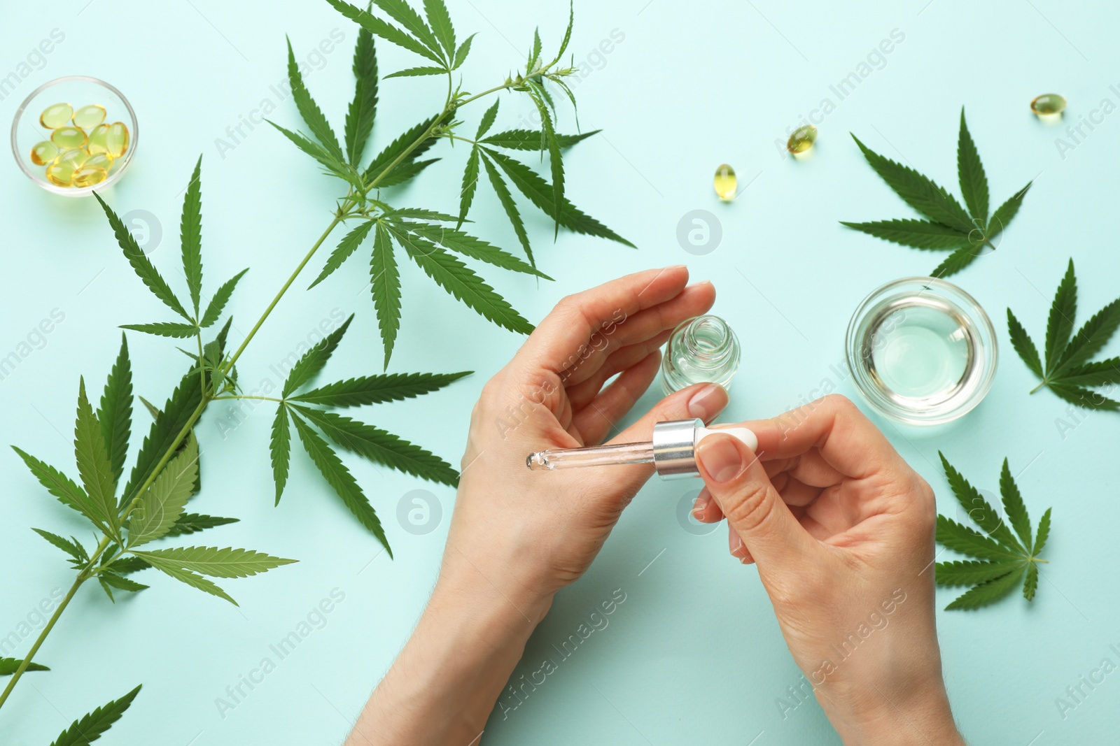 Photo of Woman applying CBD oil or THC tincture onto skin at light blue background, top view