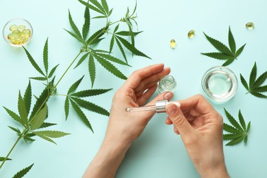 Photo of Woman applying CBD oil or THC tincture onto skin at light blue background, top view