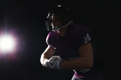 Photo of American football player wearing uniform on dark background. Space for text