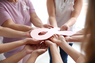 Women holding pink paper ribbon, closeup. Breast cancer awareness concept