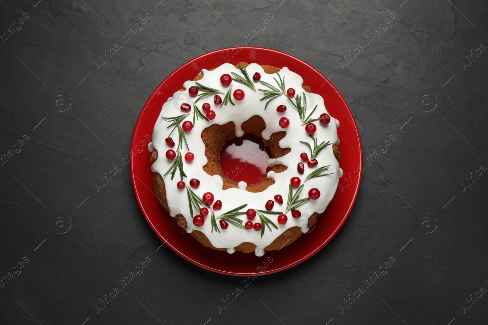 Photo of Traditional Christmas cake decorated with glaze, pomegranate seeds, cranberries and rosemary on dark grey table, top view