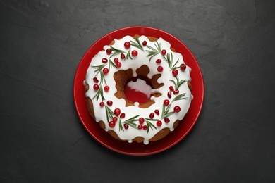 Photo of Traditional Christmas cake decorated with glaze, pomegranate seeds, cranberries and rosemary on dark grey table, top view