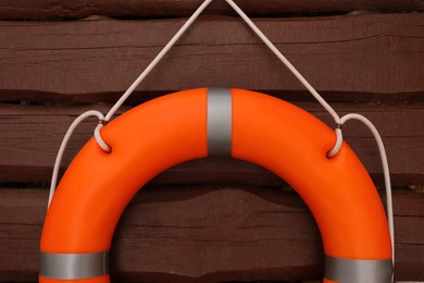 Photo of Orange lifebuoy hanging on brown wooden fence, closeup. Rescue equipment