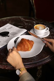 Woman with tasty croissant at black table, closeup