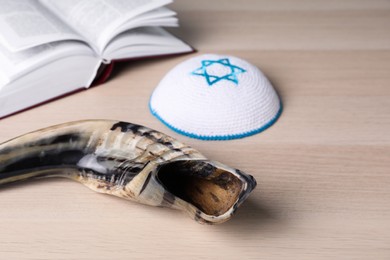Photo of Shofar and Kippah with Star of David near open Torah book on wooden table. Rosh Hashanah holiday attributes