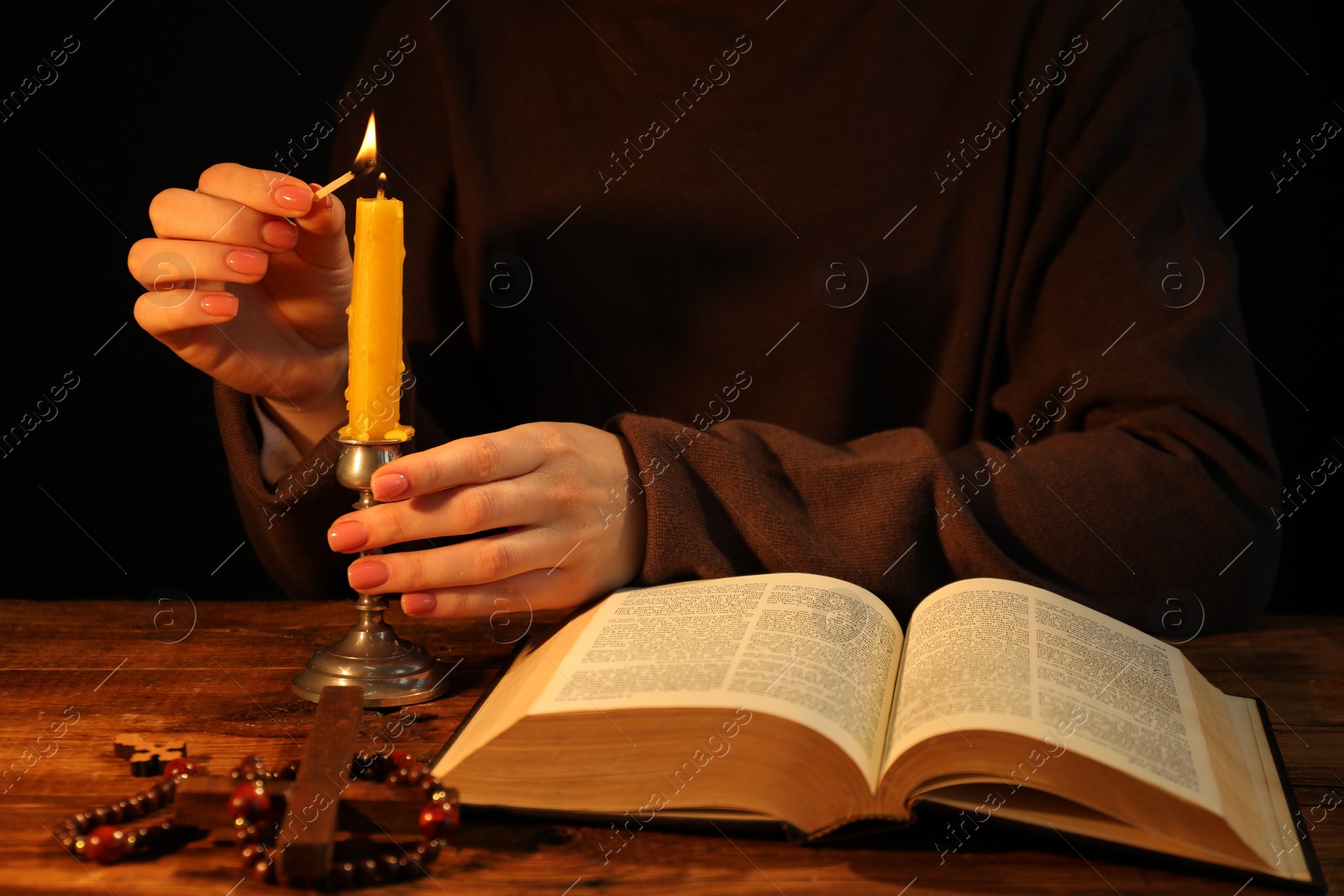 Photo of Woman lighting candle at table with Bible, closeup