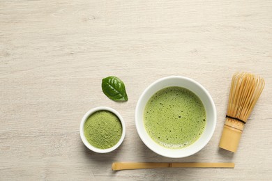Photo of Cup of fresh matcha tea, bamboo whisk, spoon and green powder on wooden table, flat lay. Space for text