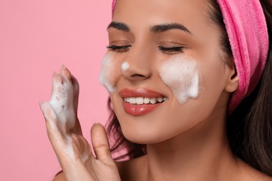 Photo of Beautiful woman applying facial cleansing foam on pink background, closeup