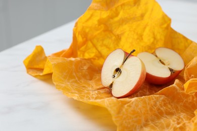 Halves of apple with orange beeswax food wrap on white table, closeup