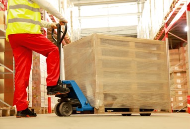 Worker moving wrapped wooden pallets with manual forklift in warehouse, closeup