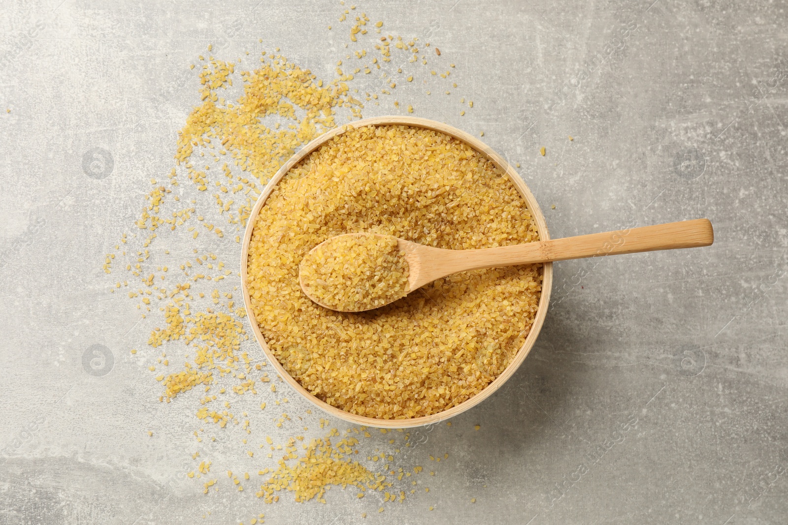 Photo of Bowl and spoon with raw bulgur on gray table, top view