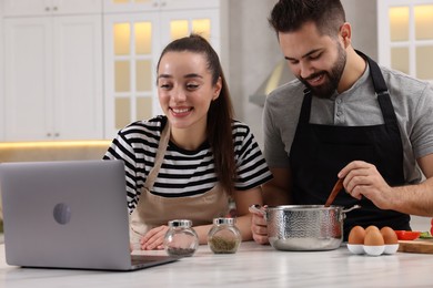 Happy lovely couple using laptop while cooking in kitchen