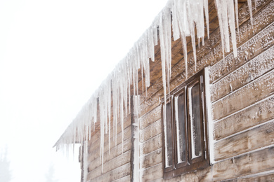 Photo of Wooden house with icicles on snowy day. Winter vacation