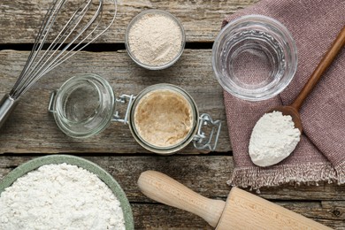 Leaven, flour, whisk, rolling pin and water on wooden table, flat lay