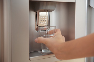 Photo of Woman filling glass with water from modern cooler, closeup
