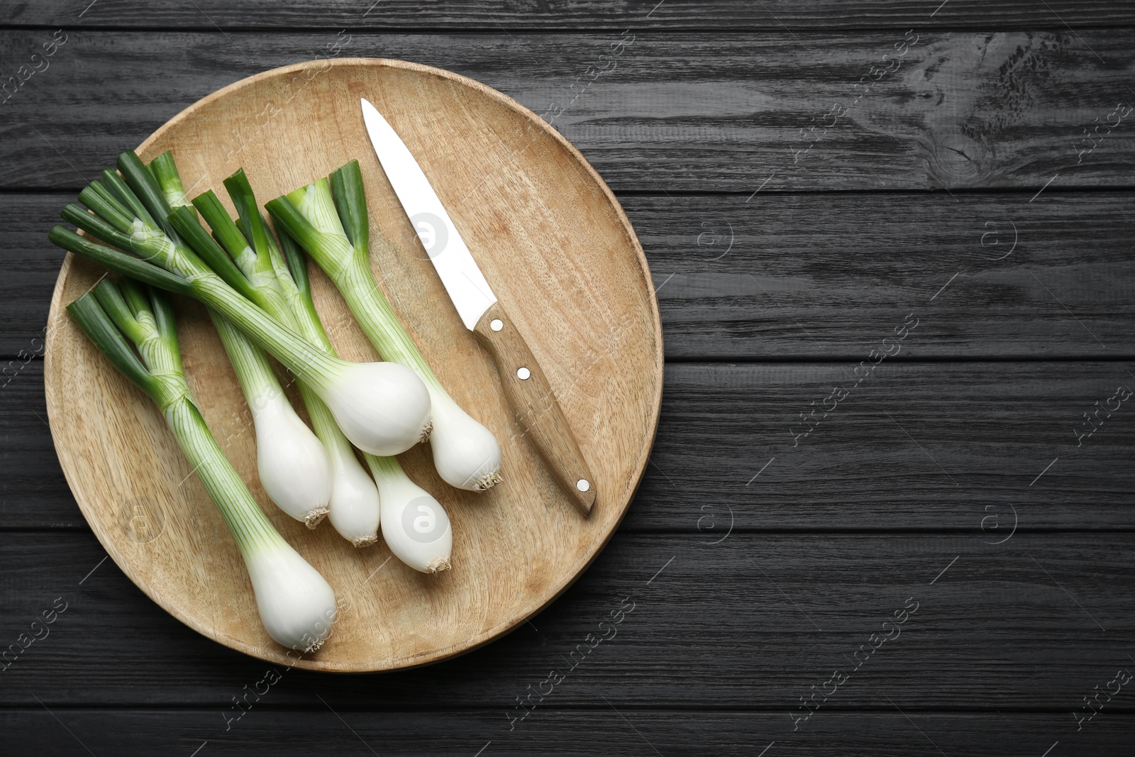 Photo of Tray with green spring onions and knife on black wooden table, top view. Space for text