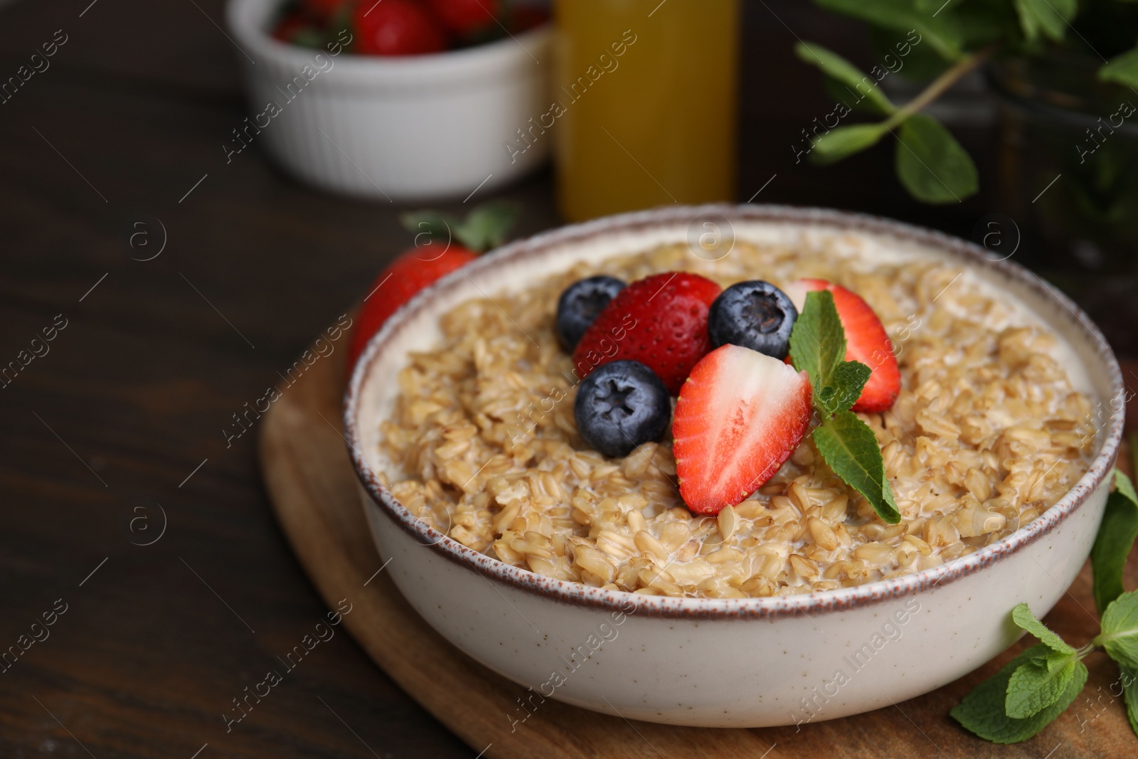 Photo of Tasty oatmeal with strawberries and blueberries in bowl on wooden table. Space for text