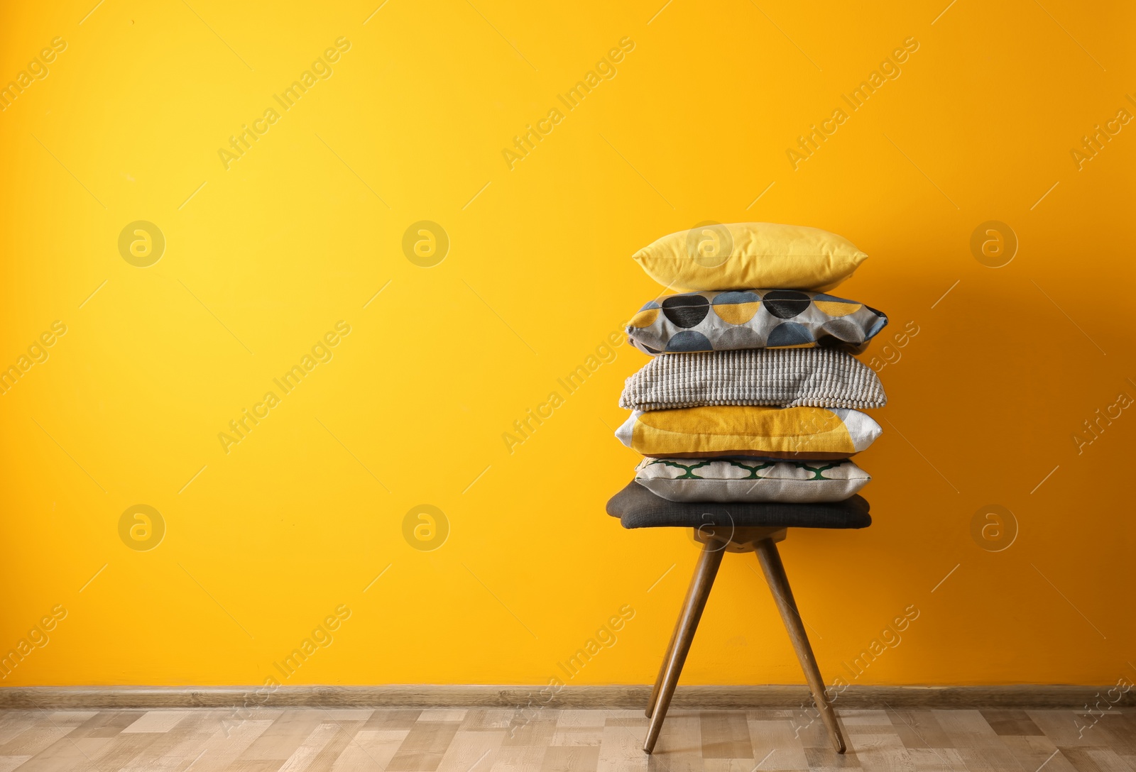 Photo of Many different pillows on chair near color wall with space for text