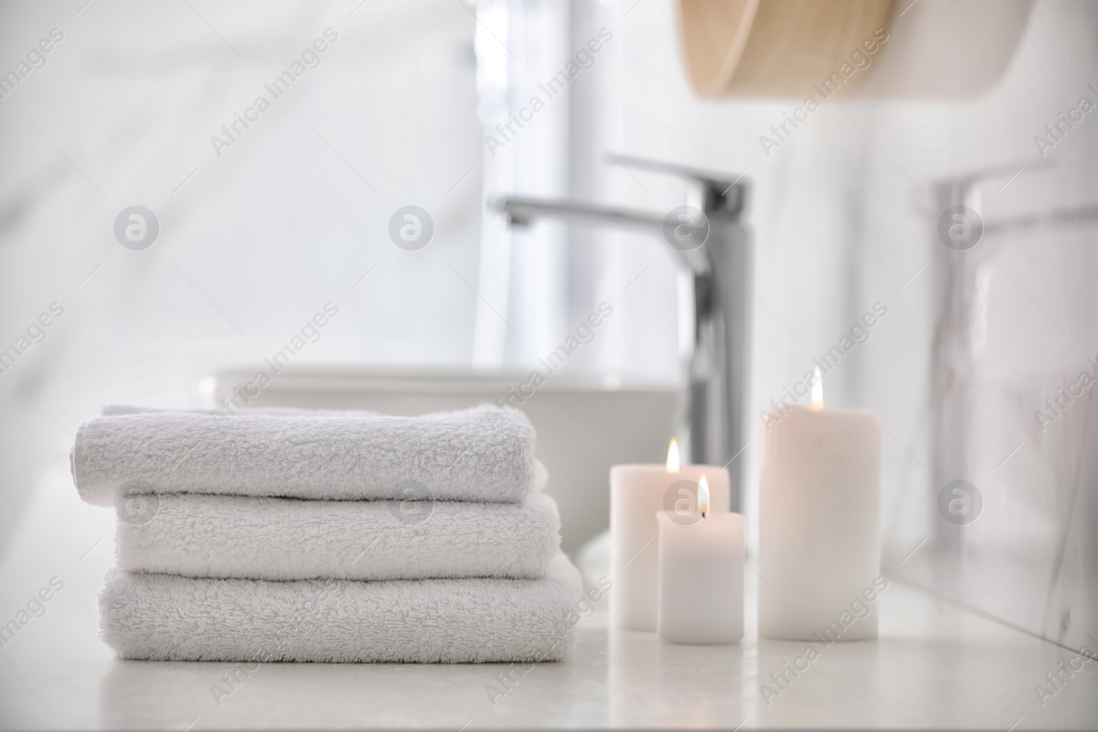 Photo of Stack of fresh towels and burning candles on countertop in bathroom