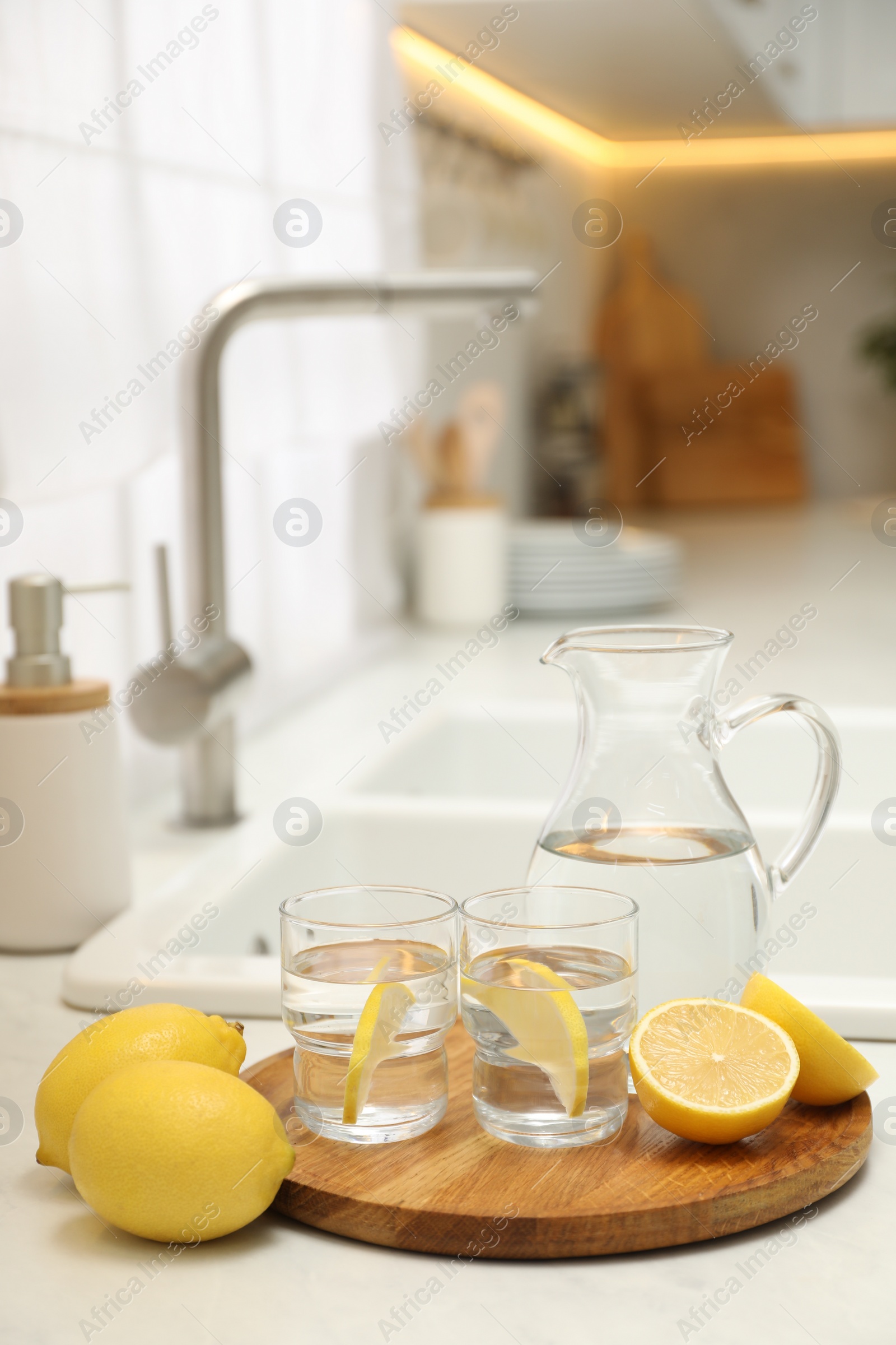 Photo of Jug, glasses with clear water and lemons on white table in kitchen