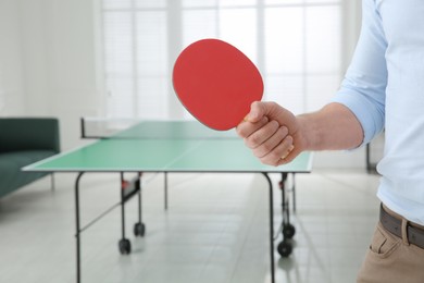 Businessman with tennis racket near ping pong table in office, closeup. Space for text