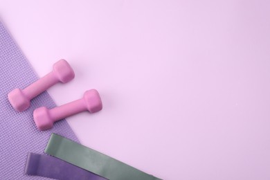 Photo of Two dumbbells, yoga mat and fitness elastic bands on violet background, flat lay. Space for text