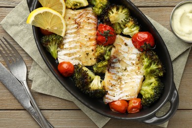 Photo of Tasty cod cooked with vegetables served on wooden table, flat lay