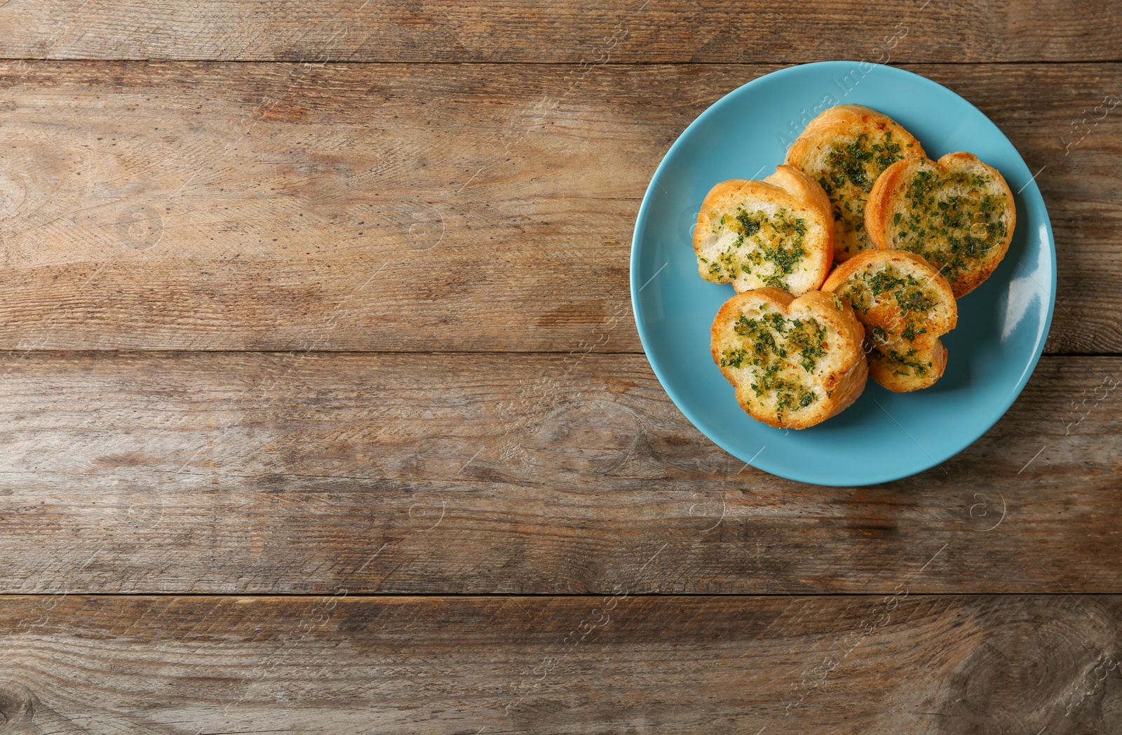 Photo of Slices of toasted bread with garlic and herbs on wooden table, top view. Space for text