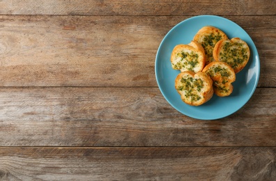 Photo of Slices of toasted bread with garlic and herbs on wooden table, top view. Space for text