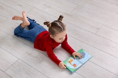 Cute little girl reading book on warm floor indoors. Heating system