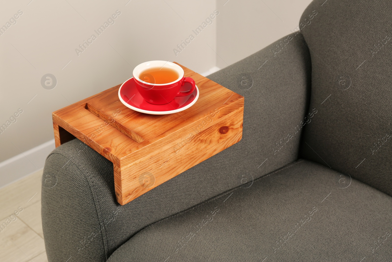 Photo of Cup of tea on sofa with wooden armrest table in room. Interior element