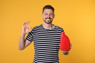 Photo of Man holding red container of motor oil and showing OK gesture on orange background