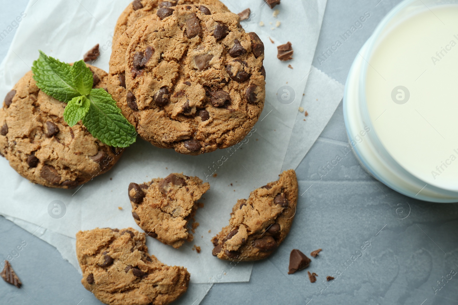 Photo of Tasty chocolate chip cookies, glass of milk and mint leaves on light grey table, flat lay